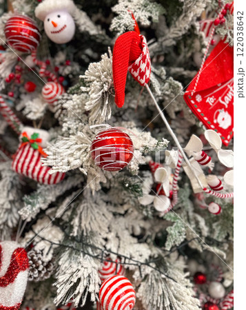 Close-up of a snow-dusted Christmas tree decorated with striped red and white ornaments. Baubles and candy canes and ribbons highlight the festive holiday atmosphere Close-up of a snow-dusted Christmas tree decorated with striped red and white ornaments. Baubles and candy canes and ribbons highlight the festive holiday atmosphere 122038642