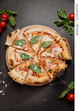 Freshly baked pizza slices with spinach, almonds, and tomatoes on a wooden board 122038755