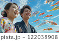 A smiling Japanese couple in traditional attire looks up at numerous colorful koi kites against a blue sky with clouds. Concept of Celebrate Golden Week in Japan or National Koi Day. 122038908