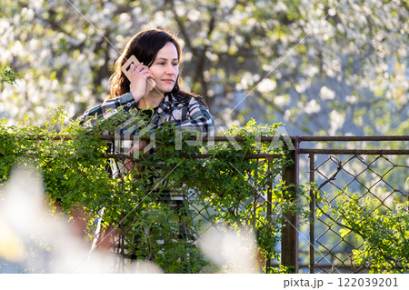 Young woman standing in spring park talking on her cellphone outdoors on warm day. Communication and mobile connection concept Young woman standing in spring park talking on her cellphone outdoors on warm day. Communication and mobile connection concept 122039201
