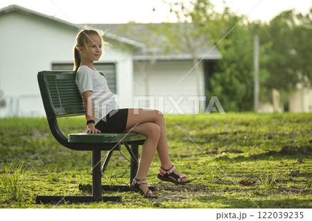 Young pretty child girl with dreamy smile resting on bench in backyard on sunny vacations day Young pretty child girl with dreamy smile resting on bench in backyard on sunny vacations day 122039235