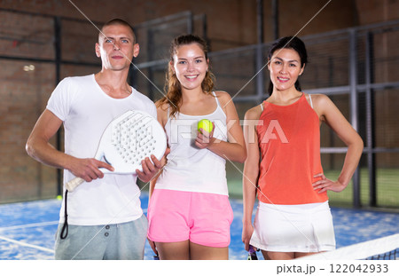 Three smiling players man and two women with padel rackets 122042933