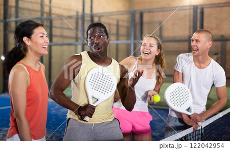 Four smiling men and women with padel rackets posing at court Four smiling men and women with padel rackets posing at court 122042954