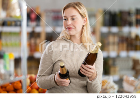 Shopping in produce supermarket - female buyer makes choice bottle of beer 122042959