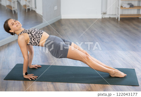 Yoga in sports gym. Girl performs side plank asana, vasishthasana Yoga in sports gym. Girl performs side plank asana, vasishthasana 122043177