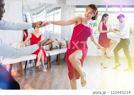 Smiling young girl in elegant clothes dancing in couple with African american man latin dance, energetic and fast jive in dance salon during celebration or party 122043214