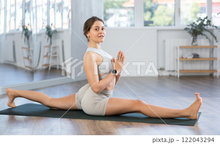 Experienced young woman yoga trainer in activewear performing split pose in gym 122043294