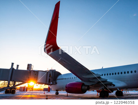 Passenger airliner near the boarding bridge on the background of sunset in winter Passenger airliner near the boarding bridge on the background of sunset in winter 122046358