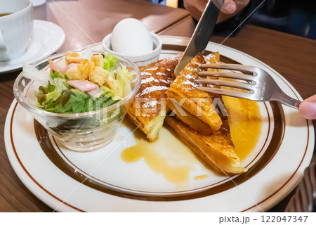 カフェで食べる朝食。甘いシロップがかかったフレンチトーストを食べてる人。 カフェで食べる朝食。甘いシロップがかかったフレンチトーストを食べてる人。 122047347
