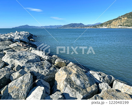 Waves of azure sea and stones. Sunny weather. Vacation in Liguria. Nature and meditation. Mountains and sun in summer.  122048199