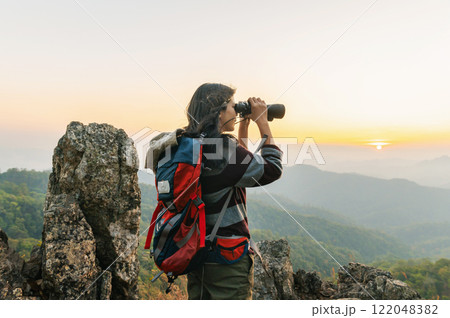 woman is standing on a mountain top, looking through a binoculars 122048382