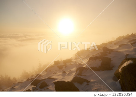 Sunrise over snow-covered mountain peak. Warm golden light of rising sun bathes clouds in soft hues of orange, pink. Sky transitions from deep blue to gentle pastel. Sunrise over snow-covered mountain peak. Warm golden light of rising sun bathes clouds in soft hues of orange, pink. Sky transitions from deep blue to gentle pastel. 122050354