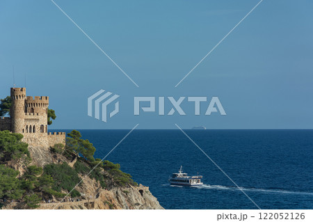 Lloret De Mar, Spain - 09/28/2019: Seascape. An old castle and a ship sailing away Lloret De Mar, Spain - 09/28/2019: Seascape. An old castle and a ship sailing away 122052126