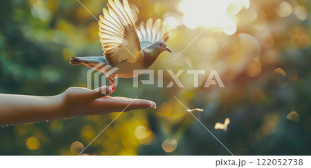 A dove taking flight from an outstretched hand, symbolizing peace, freedom, and harmony in a serene natural setting with golden sunlight A dove taking flight from an outstretched hand, symbolizing peace, freedom, and harmony in a serene natural setting with golden sunlight 122052738
