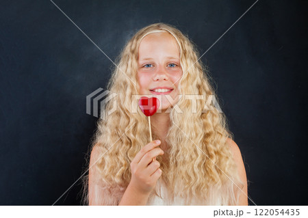 Adorable young child girl holding red heart on black background, portrait Adorable young child girl holding red heart on black background, portrait 122054435