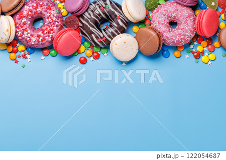 An assortment of colorful sweets, including donuts, macarons, and candies, arranged on a vibrant blue background 122054687