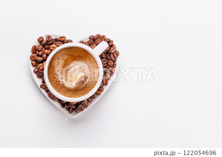 A coffee cup on a heart-shaped saucer surrounded by scattered coffee beans 122054696