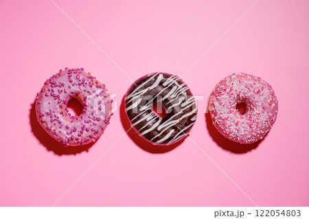 A colorful assortment of vibrant donuts with various toppings arranged on a pink A colorful assortment of vibrant donuts with various toppings arranged on a pink 122054803