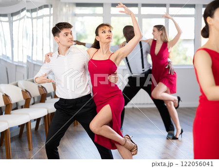 Happy young man and woman in elegant clothes performing ballroom dance in dancing room during celebration or party Happy young man and woman in elegant clothes performing ballroom dance in dancing room during celebration or party 122056041