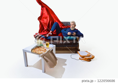 Man in superhero costume with red cape, lounging on couch with beer and snack, playing video game with game controller against white studio background Man in superhero costume with red cape, lounging on couch with beer and snack, playing video game with game controller against white studio background 122056686