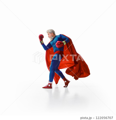 Side view image of man in superhero costume with red cape standing in boxing gloves against white studio background Side view image of man in superhero costume with red cape standing in boxing gloves against white studio background 122056707