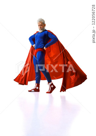 Funny man with grey hair and beard standing in blue superhero suit with red cape, executing joy against white studio background. 122056728