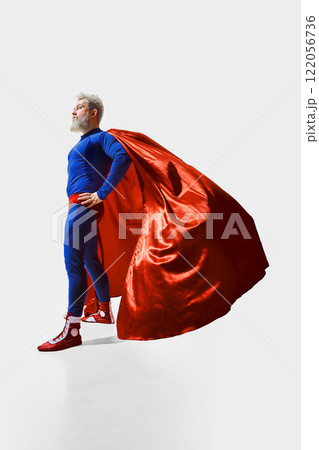 Full-length slightly low-angle view of a bearded man in image of a superhero wearing blue costume with red cape 122056736