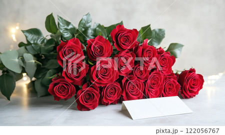 A beautiful bouquet of red roses with a handwritten Valentine Day card, displayed on a white table with elegant lighting. 122056767