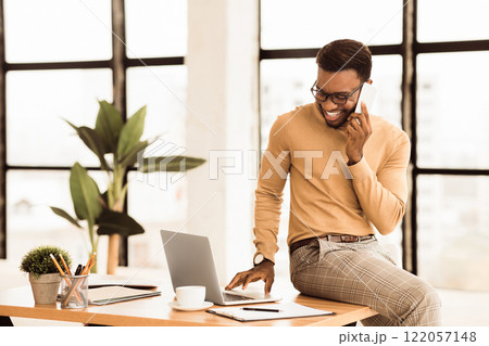 Multitasking. African businessman talking on mobile phone and using laptop. Empty space 122057148
