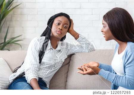 Indifference in friendship. Bored black girl tired of listening her talkative girlfriend while sitting on sofa at home together Indifference in friendship. Bored black girl tired of listening her talkative girlfriend while sitting on sofa at home together 122057293