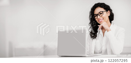 Business Concept. Happy mexican woman using laptop, watching movie, working in modern office, copyspace 122057295