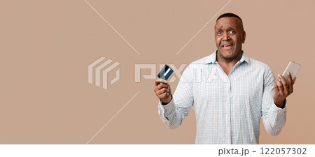 Online transaction problem. Confused middle african american man using mobile banking and credit card Online transaction problem. Confused middle african american man using mobile banking and credit card 122057302