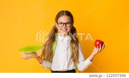 School Lunch. Happy Schoolgirl Holding Lunchbox With Sandwich And Apple Standing Over Yellow Background In Studio 122057308