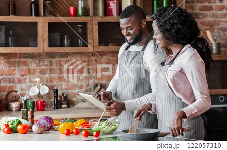 Lovely african couple using digital tablet while cooking vegetarian meal, copy space Lovely african couple using digital tablet while cooking vegetarian meal, copy space 122057310