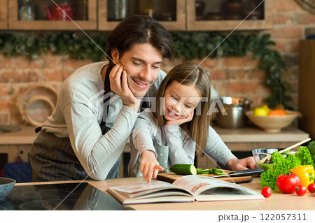 Caring young dad and little daughter searching recipe in culinary book, preparing healthy dinner together in kitchen, copy space Caring young dad and little daughter searching recipe in culinary book, preparing healthy dinner together in kitchen, copy space 122057311