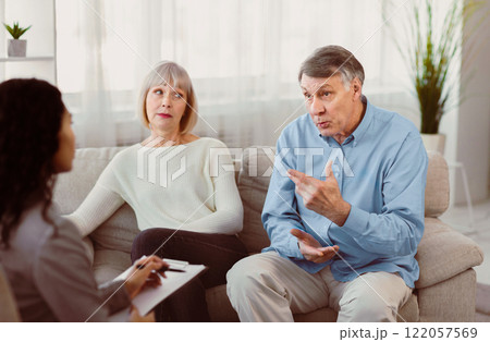 Marriage Therapist. Angry elderly husband complaining about his wife during therapy session, sitting on couch Marriage Therapist. Angry elderly husband complaining about his wife during therapy session, sitting on couch 122057569