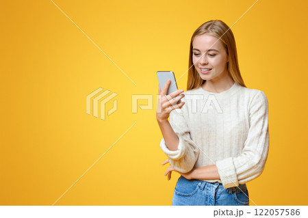 Nice App. Beautiful teen girl holding and using smartphone over orange studio background, copy space Nice App. Beautiful teen girl holding and using smartphone over orange studio background, copy space 122057586