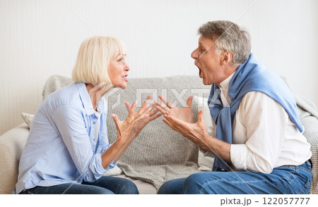Senior couple quarrelling with each other and shouting, sitting on sofa at home Senior couple quarrelling with each other and shouting, sitting on sofa at home 122057777