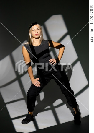 Dancer posing in studio with window light shadows, wearing black clothes Dancer posing in studio with window light shadows, wearing black clothes 122057819
