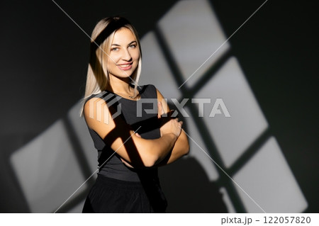 Confident businesswoman posing with arms crossed and window shadow on wall 122057820