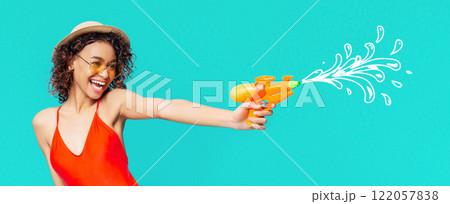 A young black woman is wearing a red swimsuit and a straw hat with sunglasses and is holding a water gun. She is smiling and aiming the water gun off to the side. 122057838