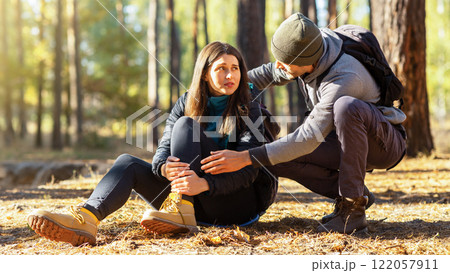 Young guy rubbing his upset girlfriend injured leg, hiking together at forest, copy space Young guy rubbing his upset girlfriend injured leg, hiking together at forest, copy space 122057911