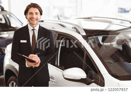 Car Vendor. Smiling sales manager standing in front of luxury auto, looking at camera, holding pen and clipboard Car Vendor. Smiling sales manager standing in front of luxury auto, looking at camera, holding pen and clipboard 122057937