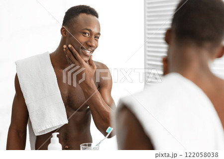 Male Facial Skincare. Cheerful African Man Touching Smooth Face After Shaving Caring For Skin Standing Near Mirror In Bathroom Indoor. Men's Beauty And Self-Care Routine Concept. Selective Focus 122058038