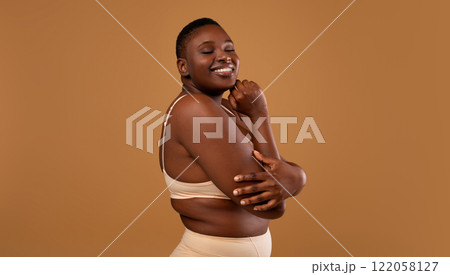Self Acceptance, Love And Care. Portrair of half-turned smiling curvy African American woman with perfect skin and closed eyes embracing herself isolated on brown studio background, free copy space Self Acceptance, Love And Care. Portrair of half-turned smiling curvy African American woman with perfect skin and closed eyes embracing herself isolated on brown studio background, free copy space 122058127