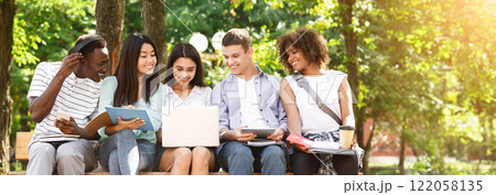 Learning Concept. Group Of College Friends With Laptop Preparing For Lessons Together, Sitting On Bench In Campus Learning Concept. Group Of College Friends With Laptop Preparing For Lessons Together, Sitting On Bench In Campus 122058135