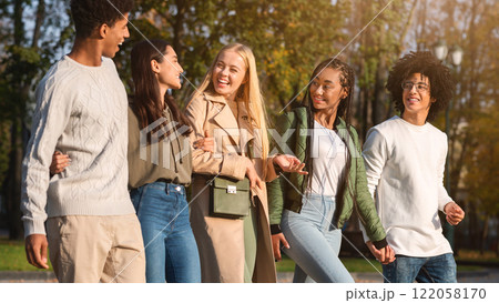 Side view of cheerful international friends spending time together outdoors, walking and talking 122058170