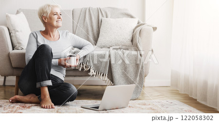 Cheerful elderly business lady sitting on floor at home, drinking coffee, using laptop, free space 122058302