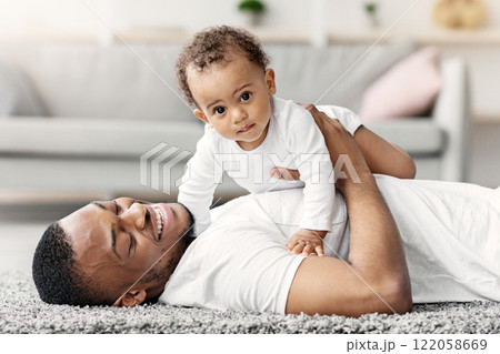 Adorable Cute Baby Boy Lying On Father's Chest While They Relaxing At Home Together, Happy African American Dad Spending Time With His Male Infant Child, Enjoying Paternity Leave, Closeup Adorable Cute Baby Boy Lying On Father's Chest While They Relaxing At Home Together, Happy African American Dad Spending Time With His Male Infant Child, Enjoying Paternity Leave, Closeup 122058669