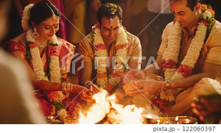 A couple engages in a sacred wedding ritual, surrounded by family and friends, as they offer prayers to the fire. 122060397